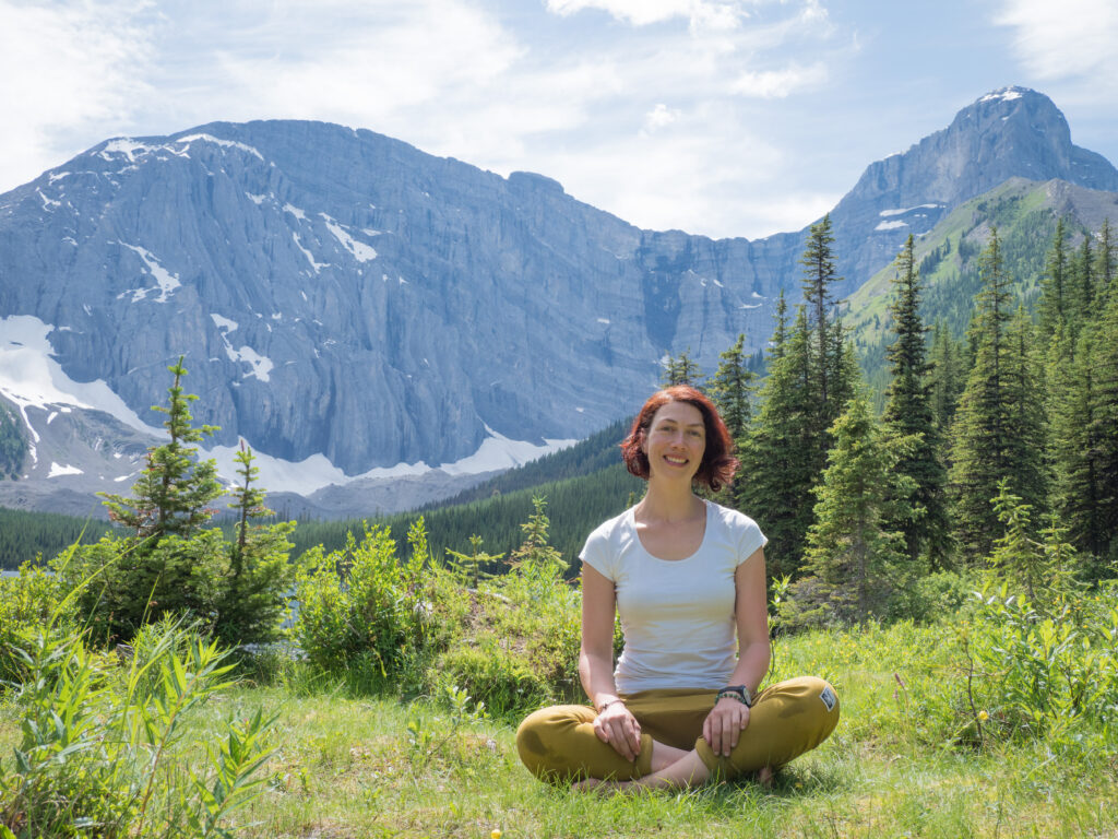 Ayla Kiser sitting in a green field in the Canadian Rocky Mountains